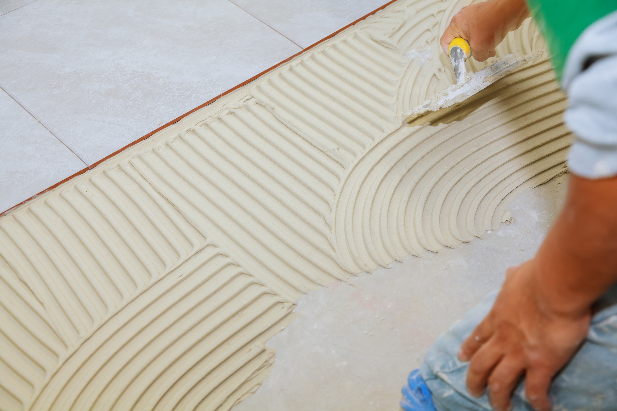 Master puts adhesive Spreading wet mortar before applying tiles on bathroom floor.
