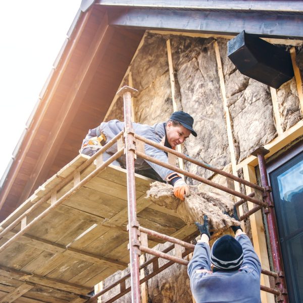 Construction workers thermally insulating house facade with glass wool.