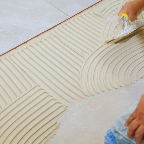 Master puts adhesive Spreading wet mortar before applying tiles on bathroom floor.